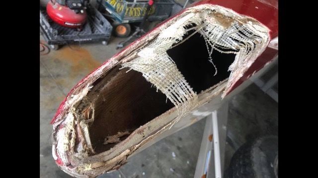 Damaged red car panel with a large hole revealing inner structure and white fabric.