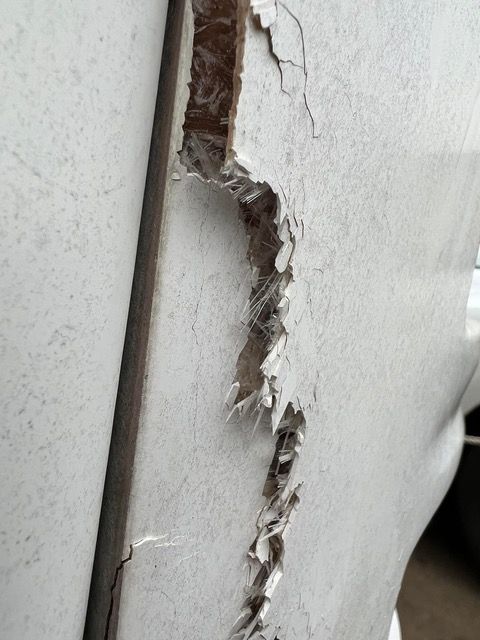 Damaged white surface with a large crack revealing fibrous material.