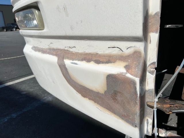Close-up of a vehicle's white bumper with visible patches of repair work.