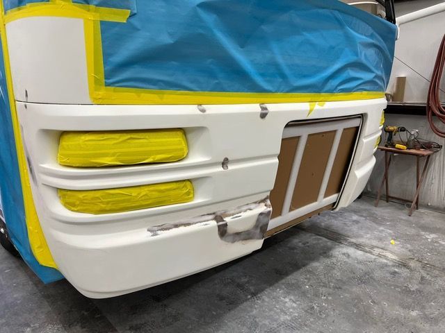 White rv bumper being repaired, taped off for painting.
