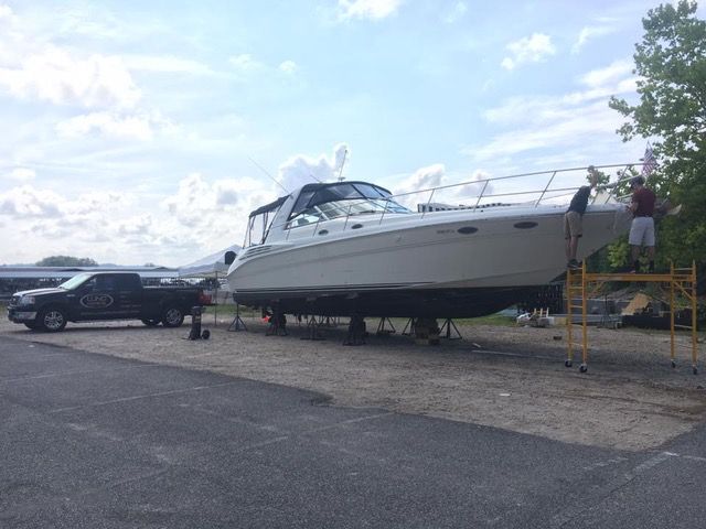 A large boat on supports, workers nearby, next to a truck.