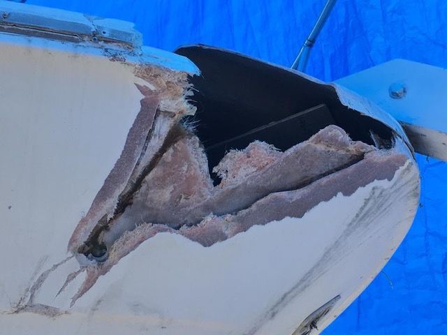 Damaged boat hull with exposed fiberglass and chipped paint against a blue tarp.