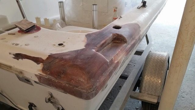 Boat hull undergoing repair, with visible filled areas in brown, resting on a trailer.
