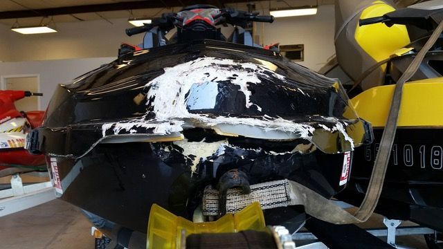 Damaged black jet ski with white material exposed, potentially showing impact.