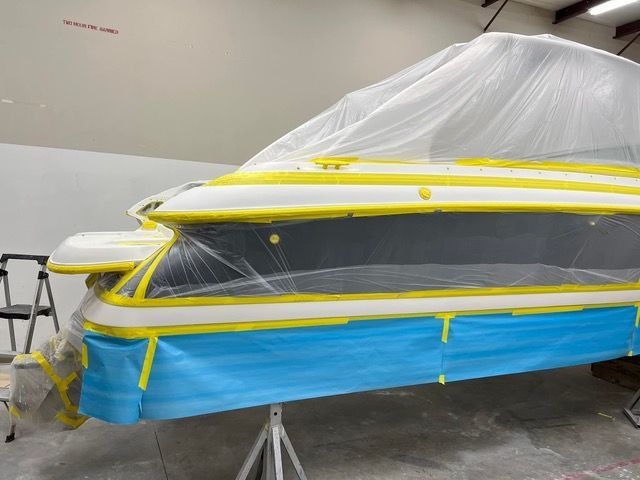 Boat being prepped for painting with yellow tape and blue masking paper in a workshop.