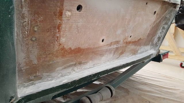 Close-up of boat hull shows exposed wood and white coating, with green painted sides.