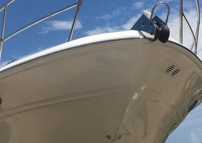 White boat bow with stainless steel railing and anchor against a blue sky.