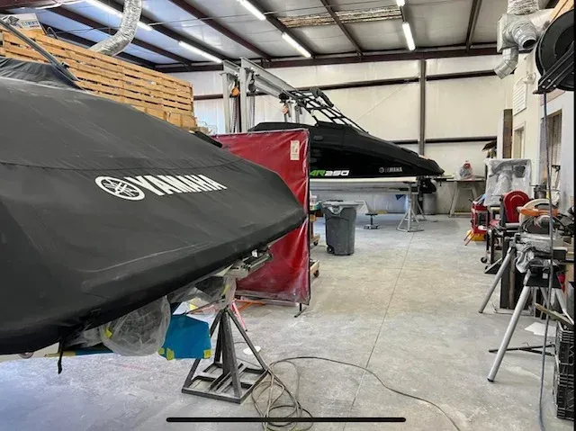 Inside a repair shop, two covered watercraft, Yamaha logo visible. Equipment and tools.