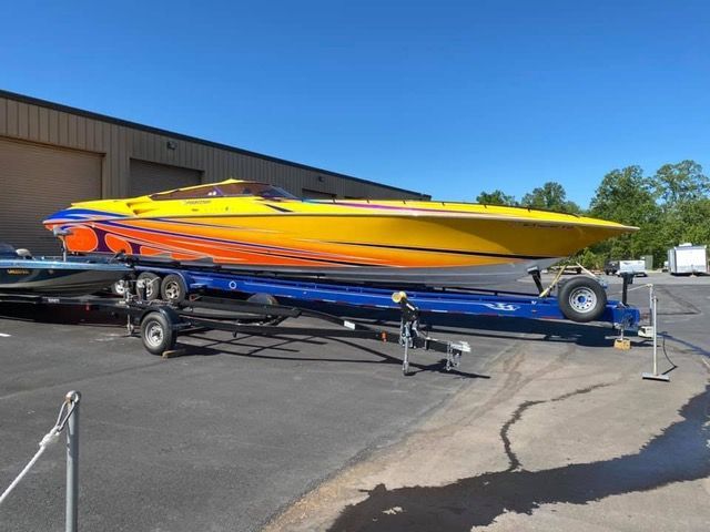 Yellow and orange speed boat on a blue trailer, parked outside a building on a sunny day.