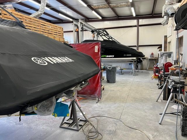 Yamaha covered watercraft in a workshop. Red paint booth, tools, and a person working in the background.
