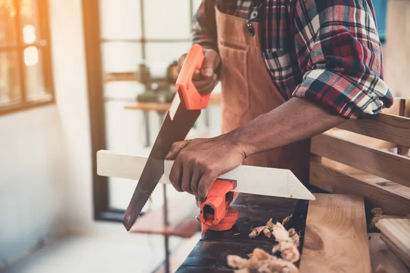 The Handyman Winnipeg using a circular saw to cut a wooden plank in a workshop; sawdust visible.