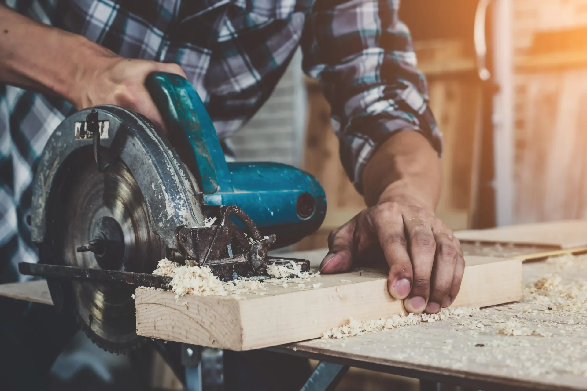 The Handyman Winnipeg using a circular saw to cut a wooden plank in a workshop; sawdust visible.