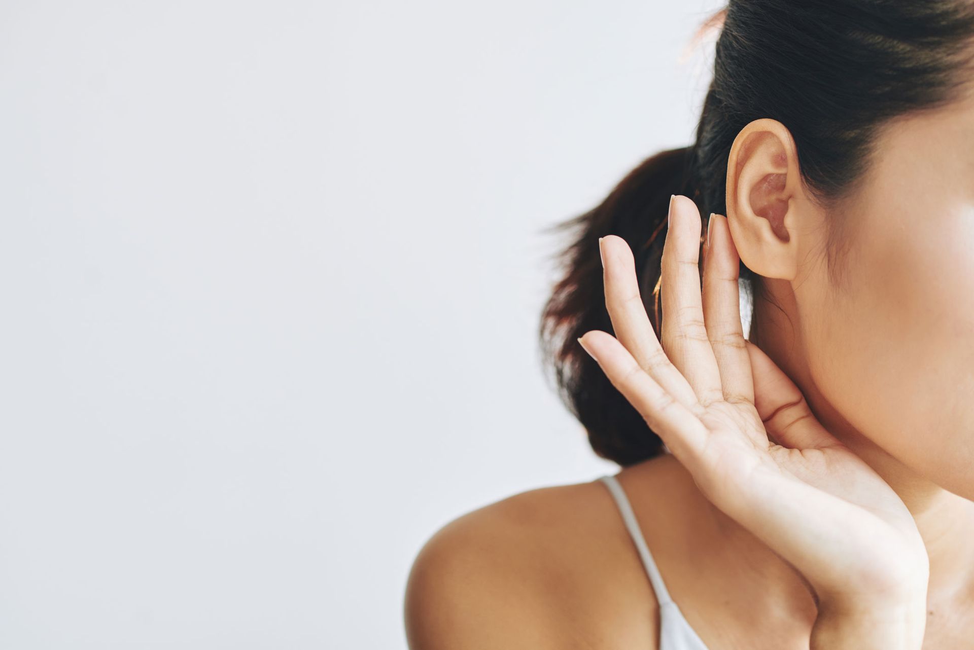 Close-up of a person cupping their ear, wearing a white strap, against a light background