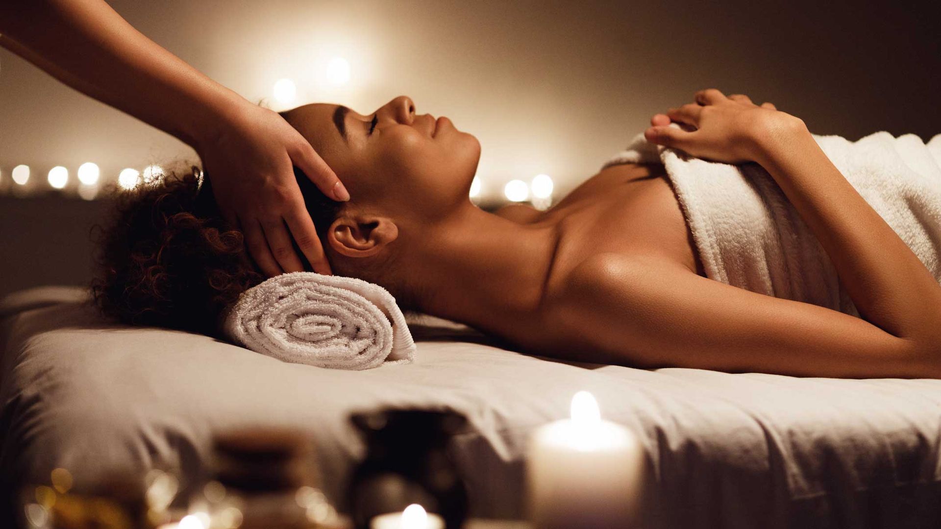 Person receiving a spa massage with candles and warm, dim lighting