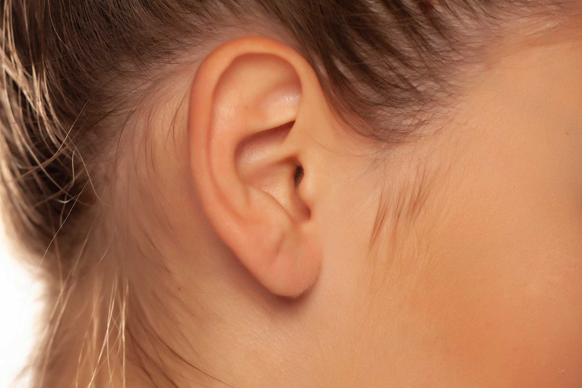 Close-up of a person's ear and side of face with brown hair pulled back