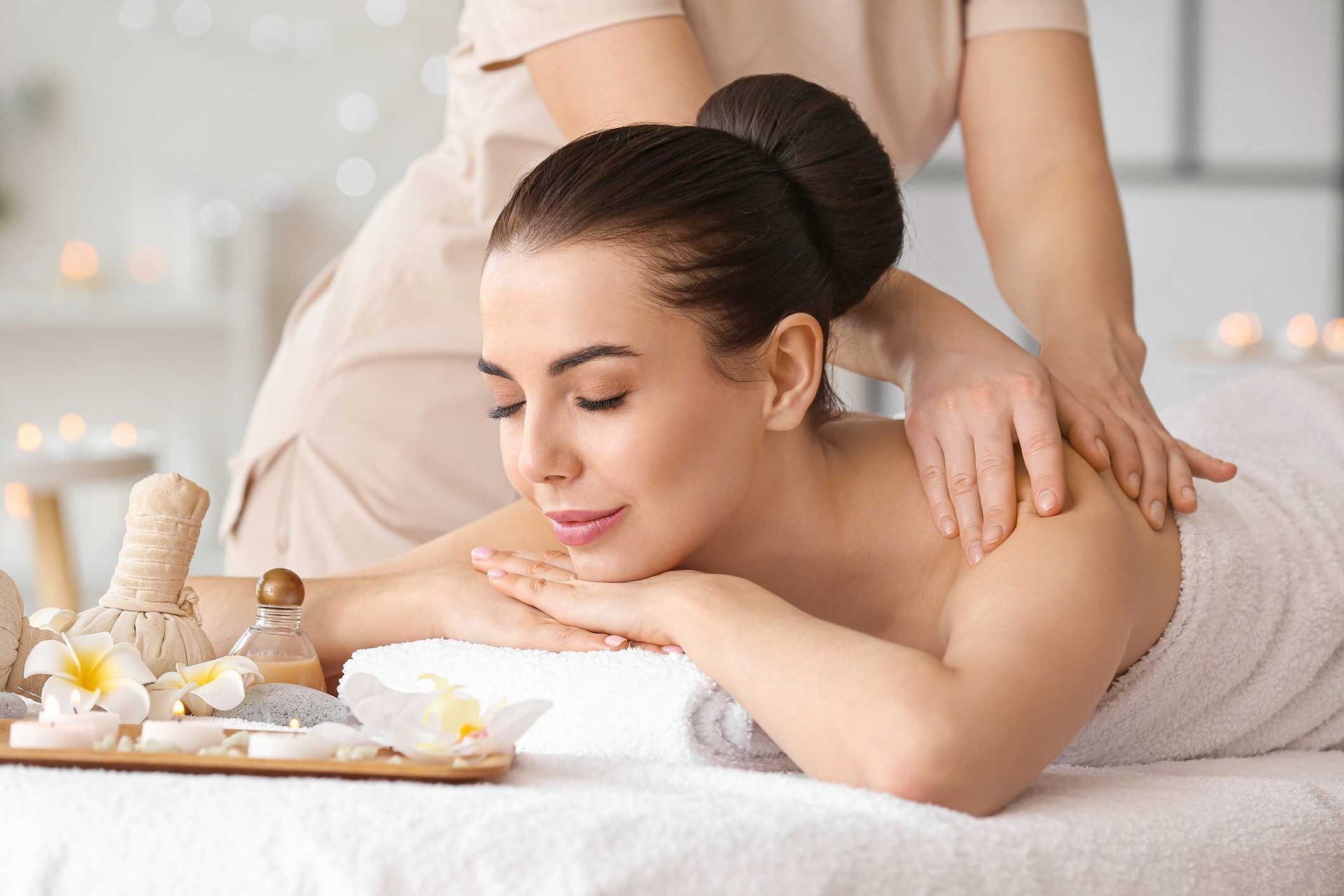 Woman receiving a back massage in a spa, with candles and towels on a soft white table