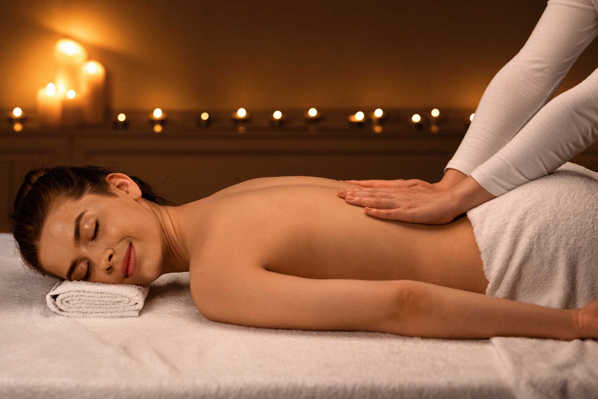 Person receiving a back massage on a spa table with candles in the background