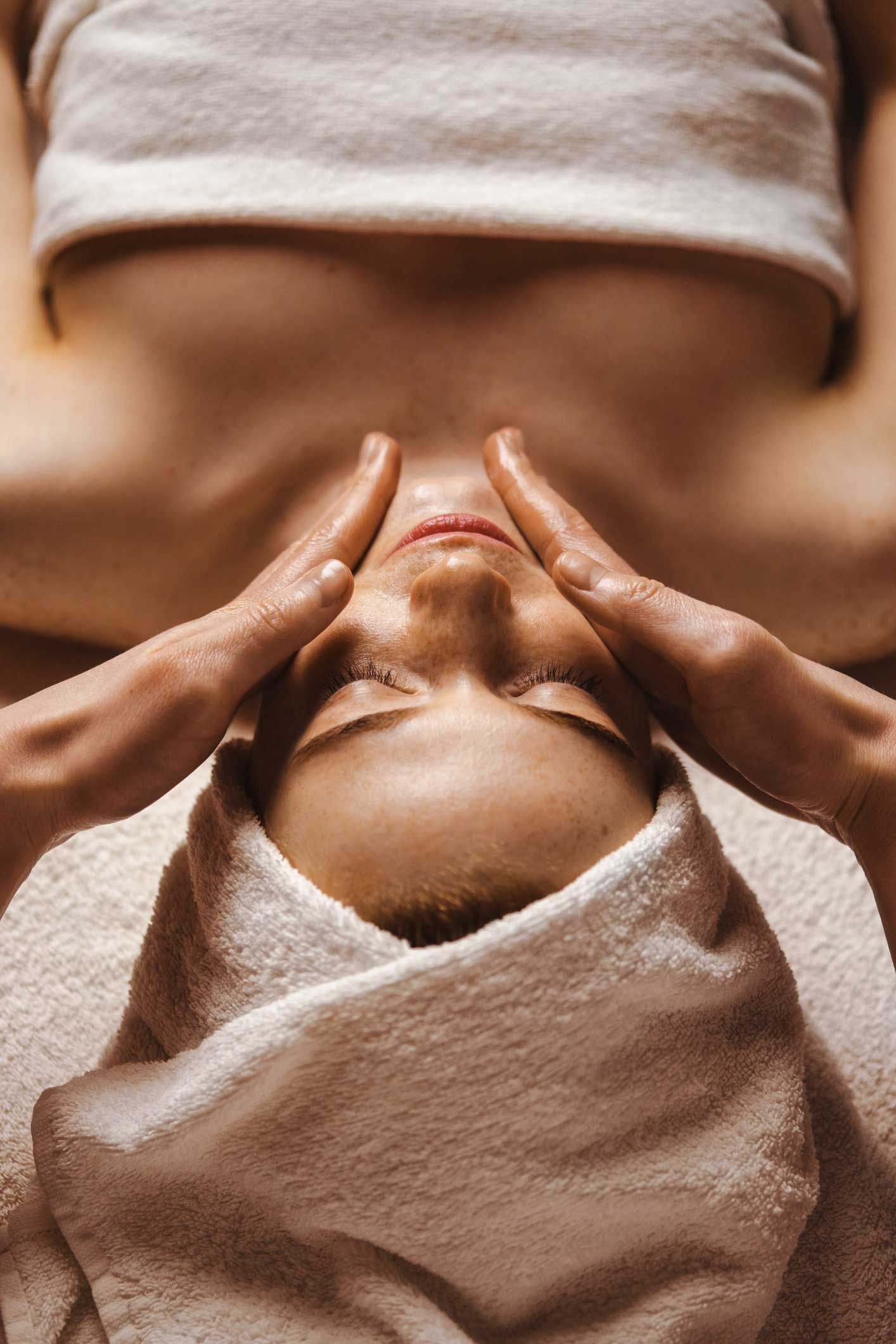 Person receiving a facial massage with towel head wrap, lying on a spa bed