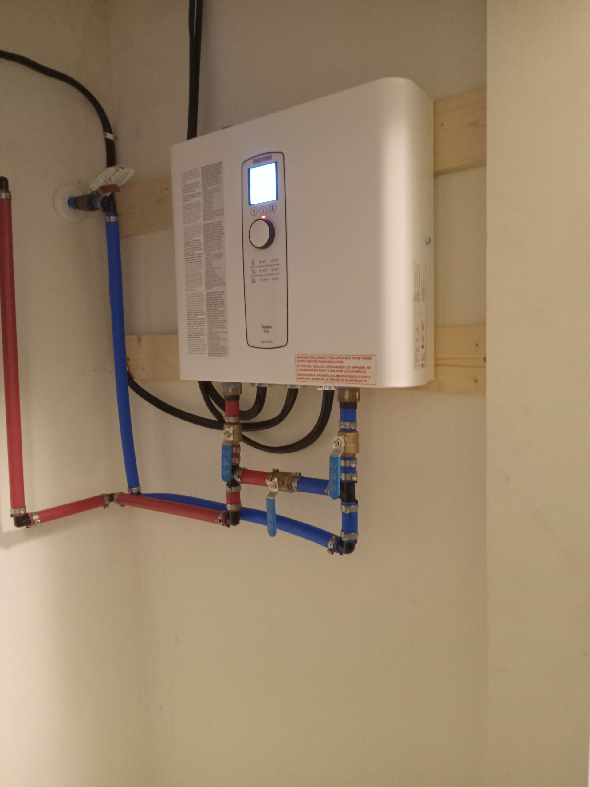 A water heater is attached to a wall with blue and red pipes