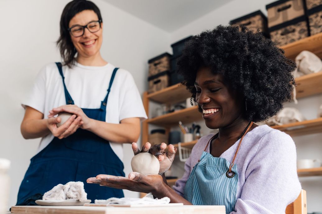 Two women are sitting at a table making clay pots.