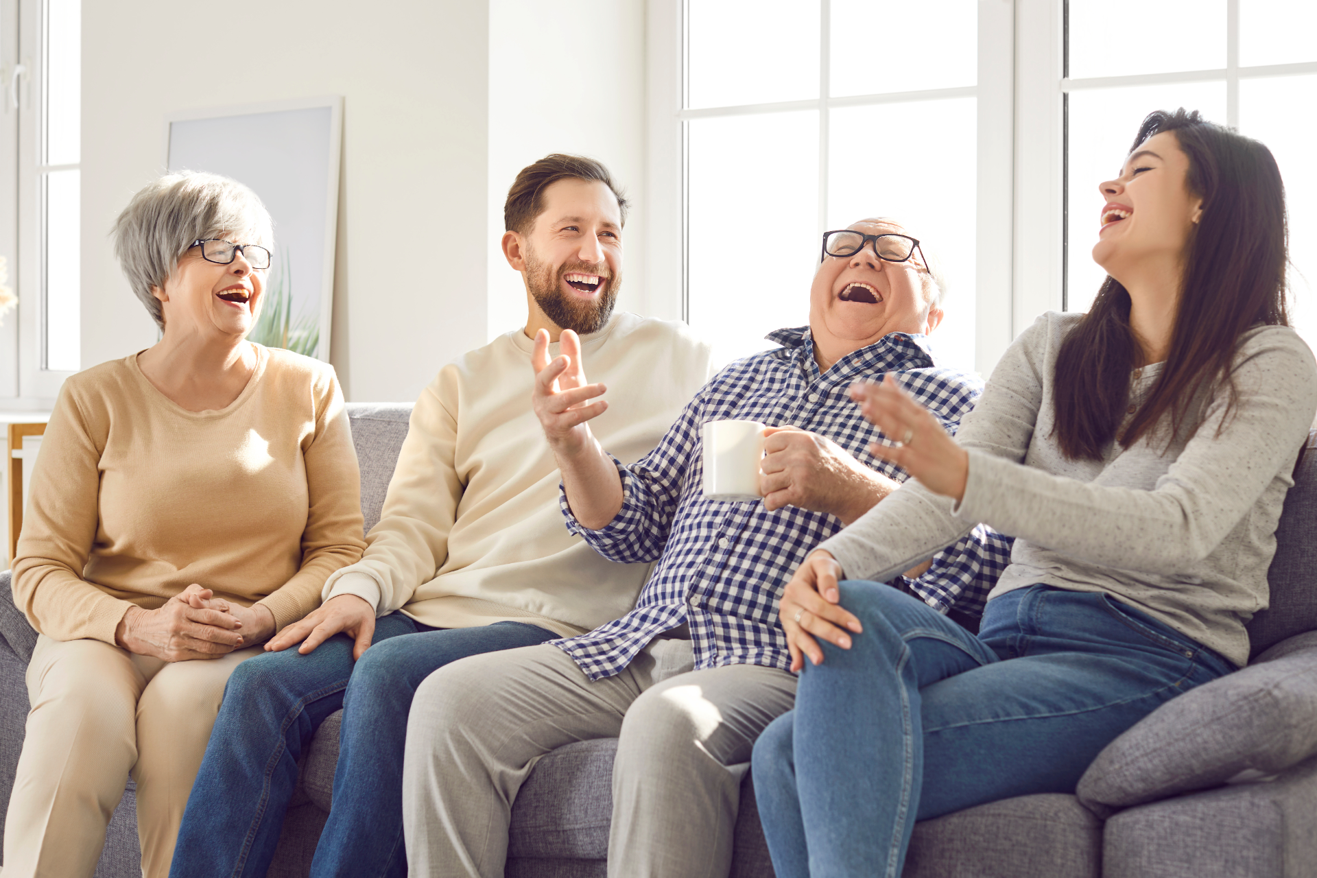 Family of four laughing together on a gray couch near a window.