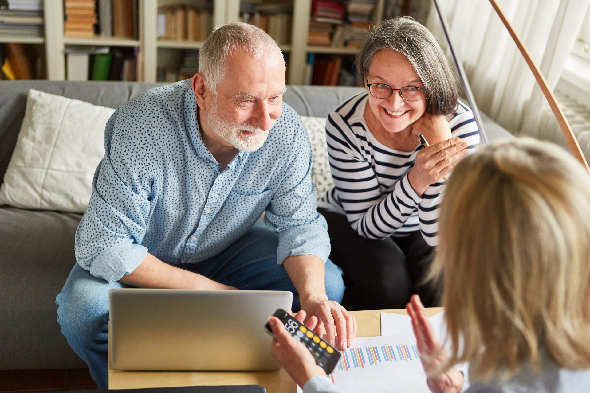 Senior couple meeting with a financial advisor in their living room, looking at a laptop and documents.