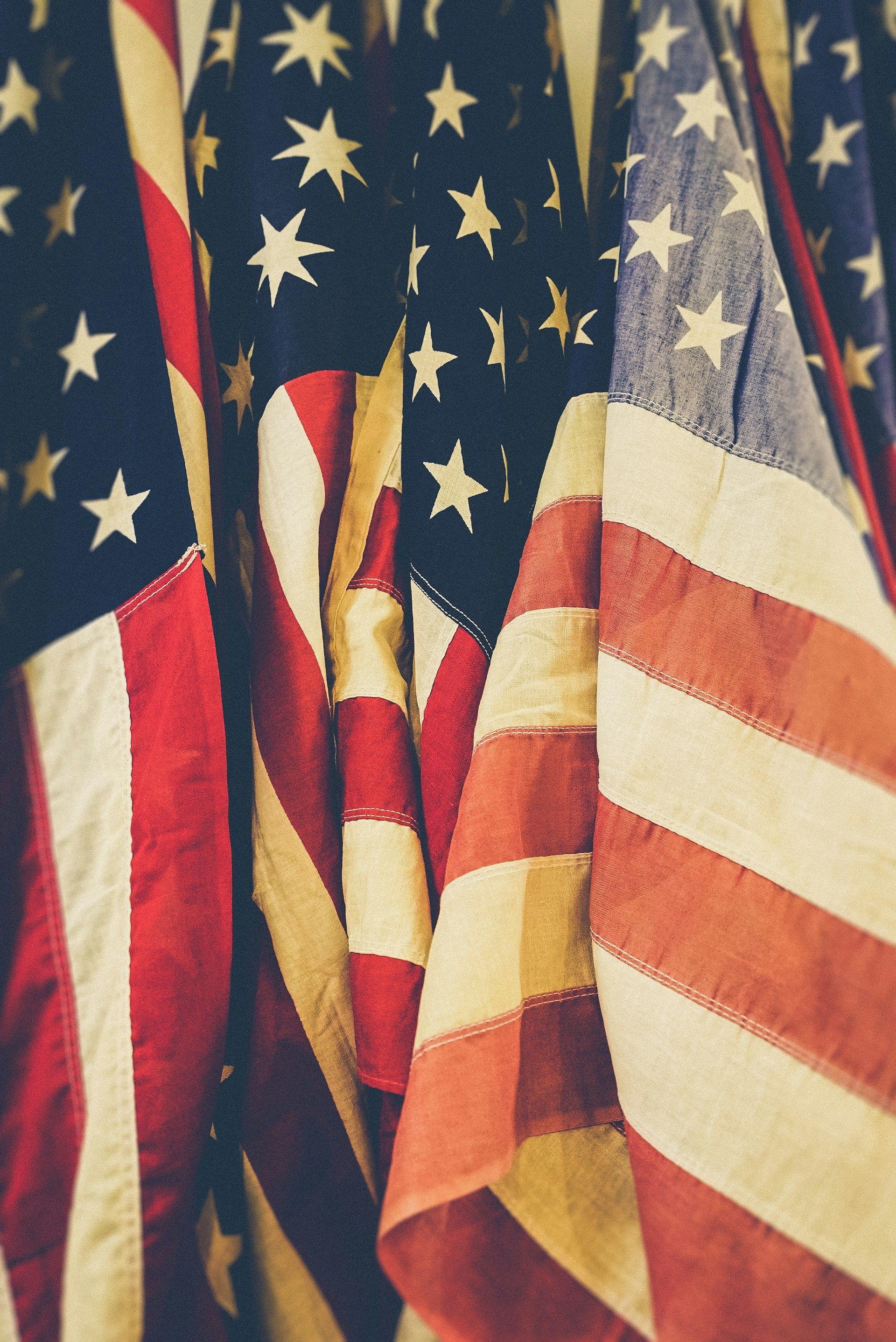 Close-up of American flags, displaying stars and stripes in red, white, and blue, with a weathered appearance.