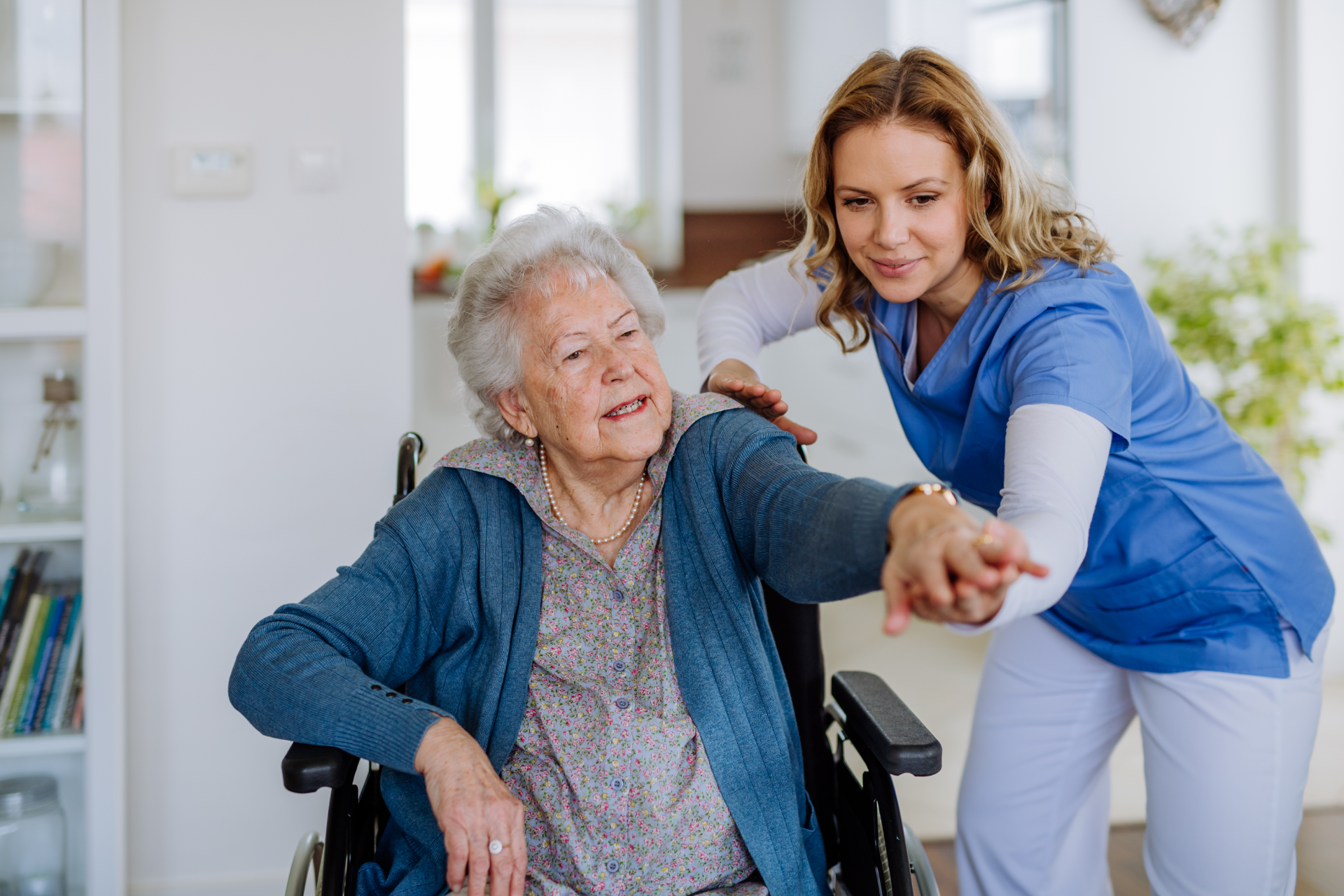Caregiver assisting elderly woman in wheelchair, smiling, indoors.