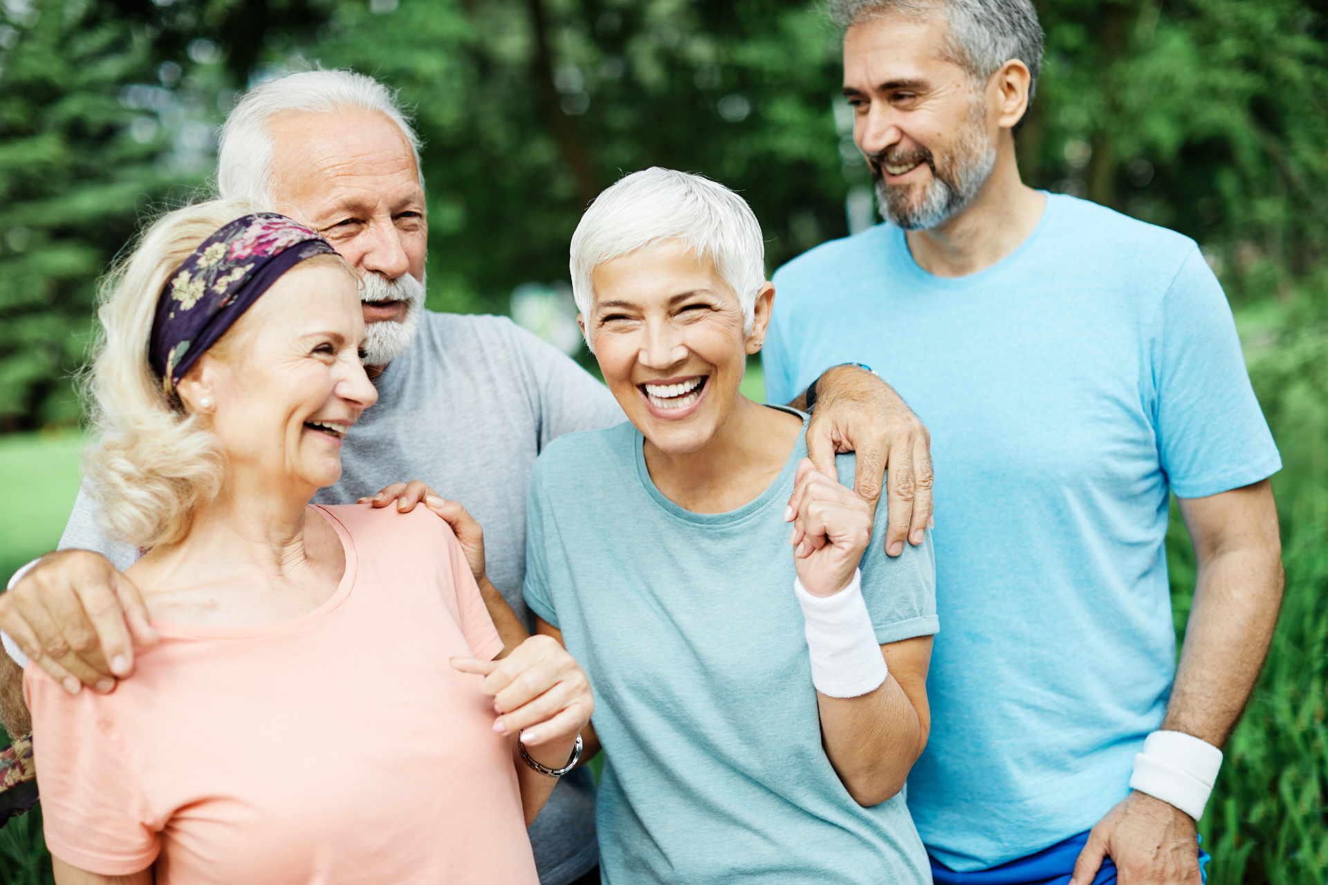 Four older adults smiling together outdoors; a man has his arm around two women.