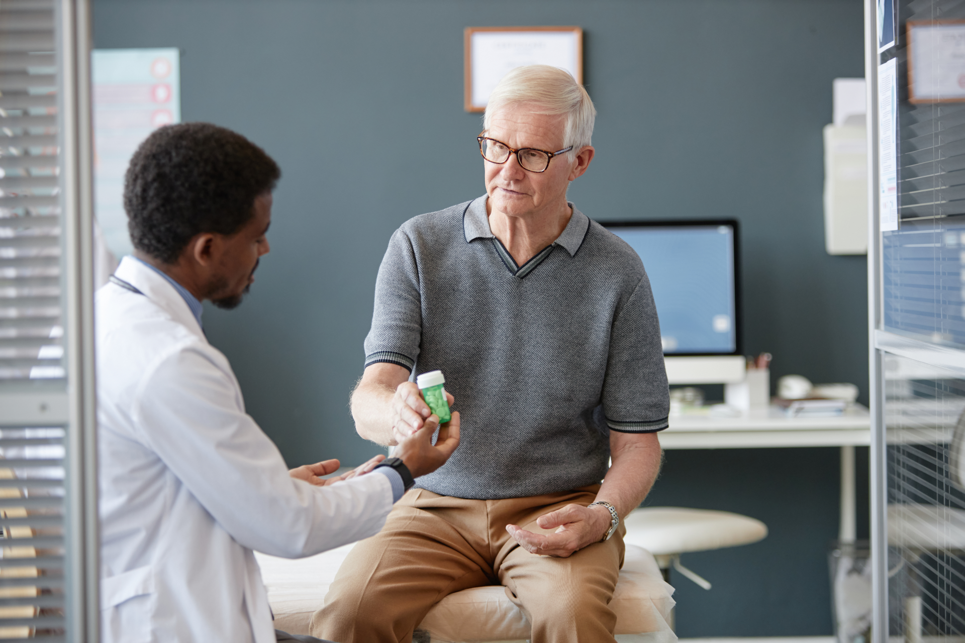 Doctor handing a pill bottle to an elderly patient in an office setting.