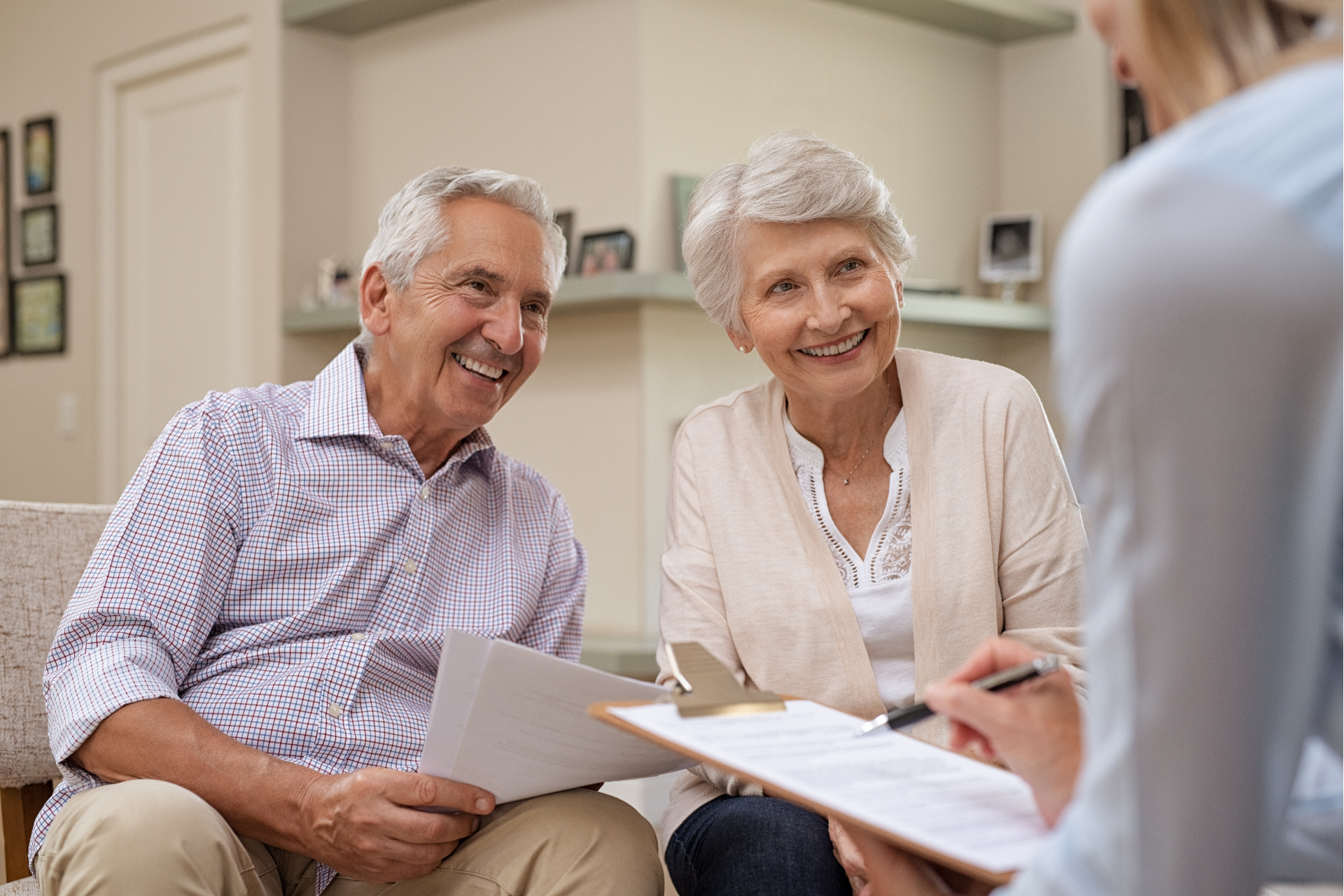 Smiling senior couple consulting with a person holding a clipboard in a well-lit living room.