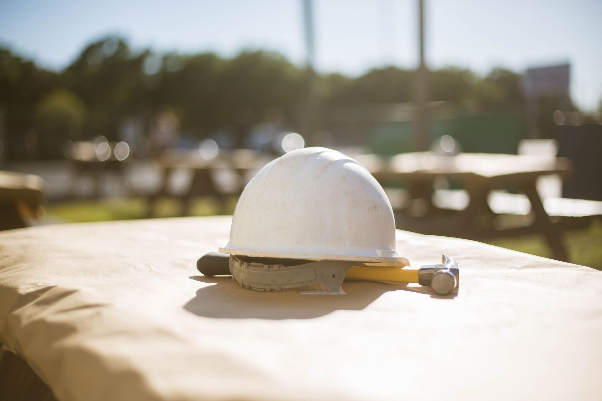 Casco bianco da cantiere su un tavolo all'aperto, in piena luce solare, con sfondo sfocato.