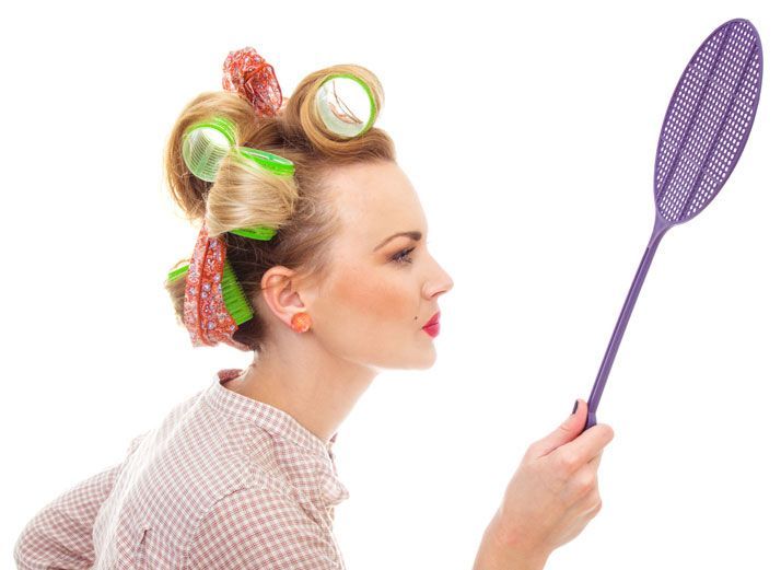 A woman with curlers in her hair is holding a fly swatter