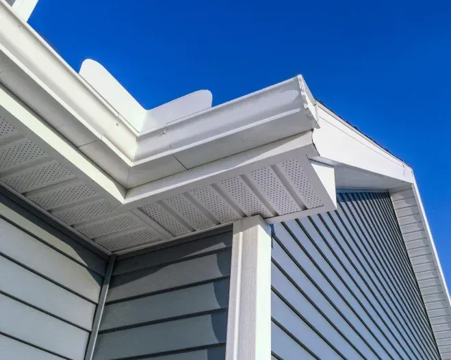 A white gutter on the side of a house with a blue sky in the background.