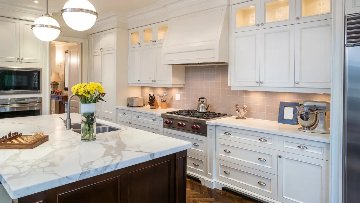 A kitchen with white cabinets , marble counter tops , stainless steel appliances and a large island.