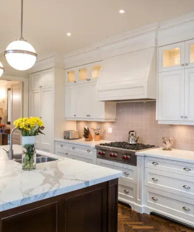 A kitchen with white cabinets , a stove , a sink , and a vase of flowers on the counter.
