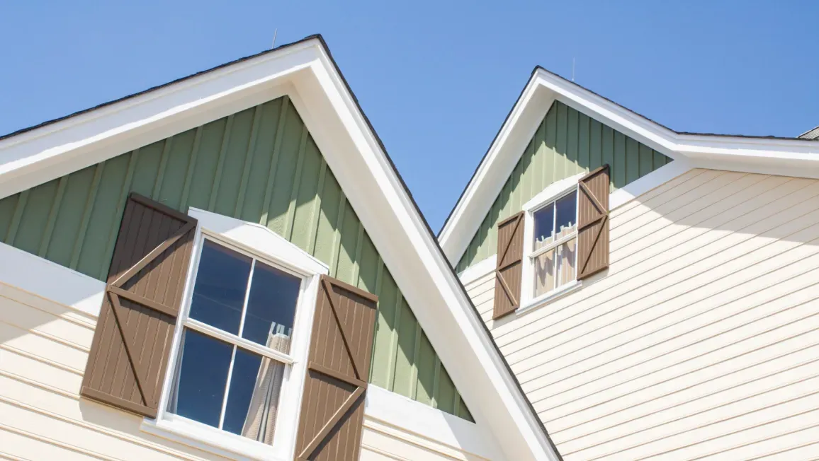 Two houses with green siding and brown shutters are sitting next to each other.