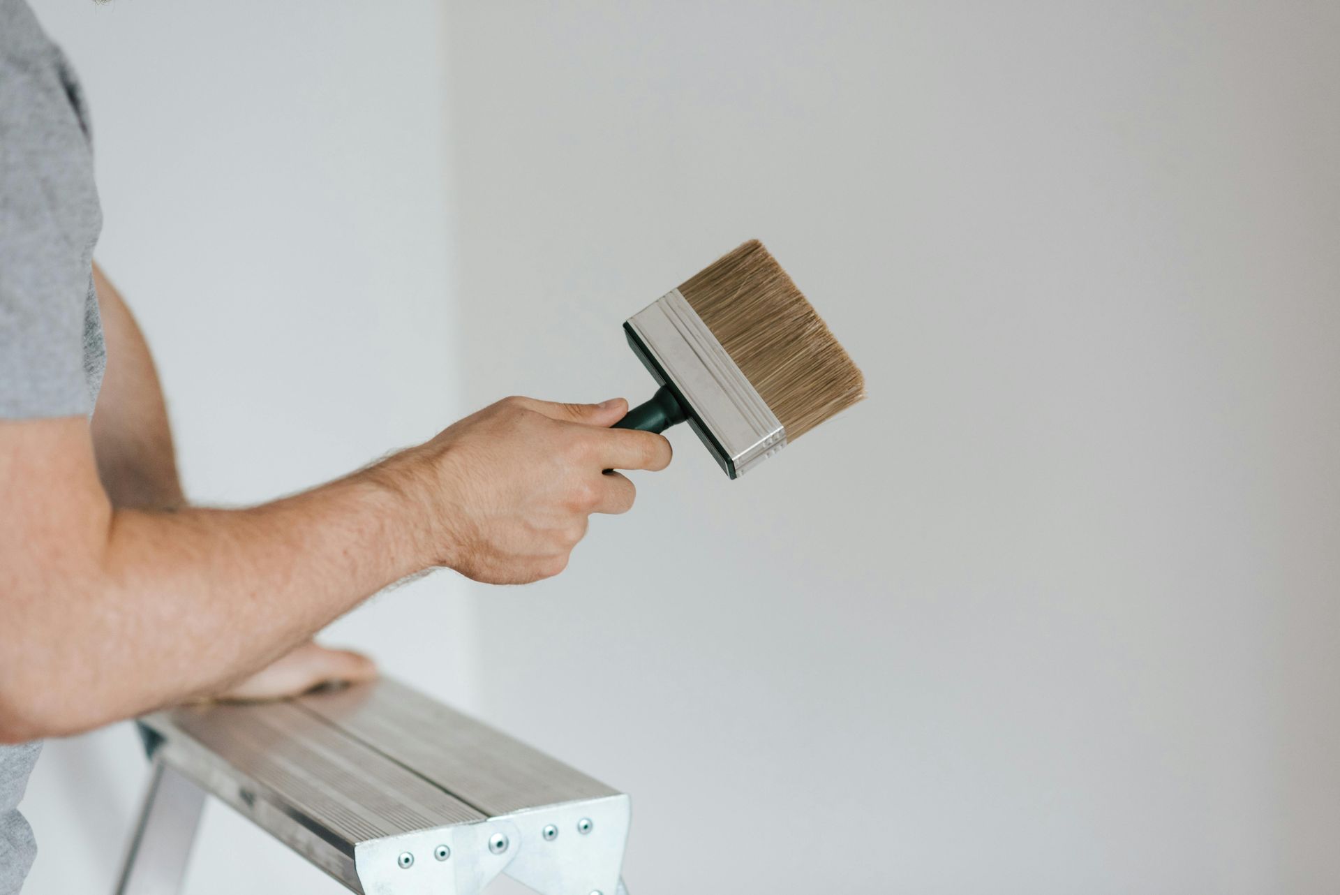 A man is standing on a ladder holding a paint brush.
