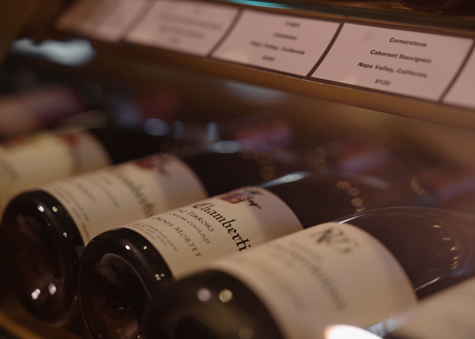 Several bottles of wine are lined up on a shelf and one of them has a label that says gambetti