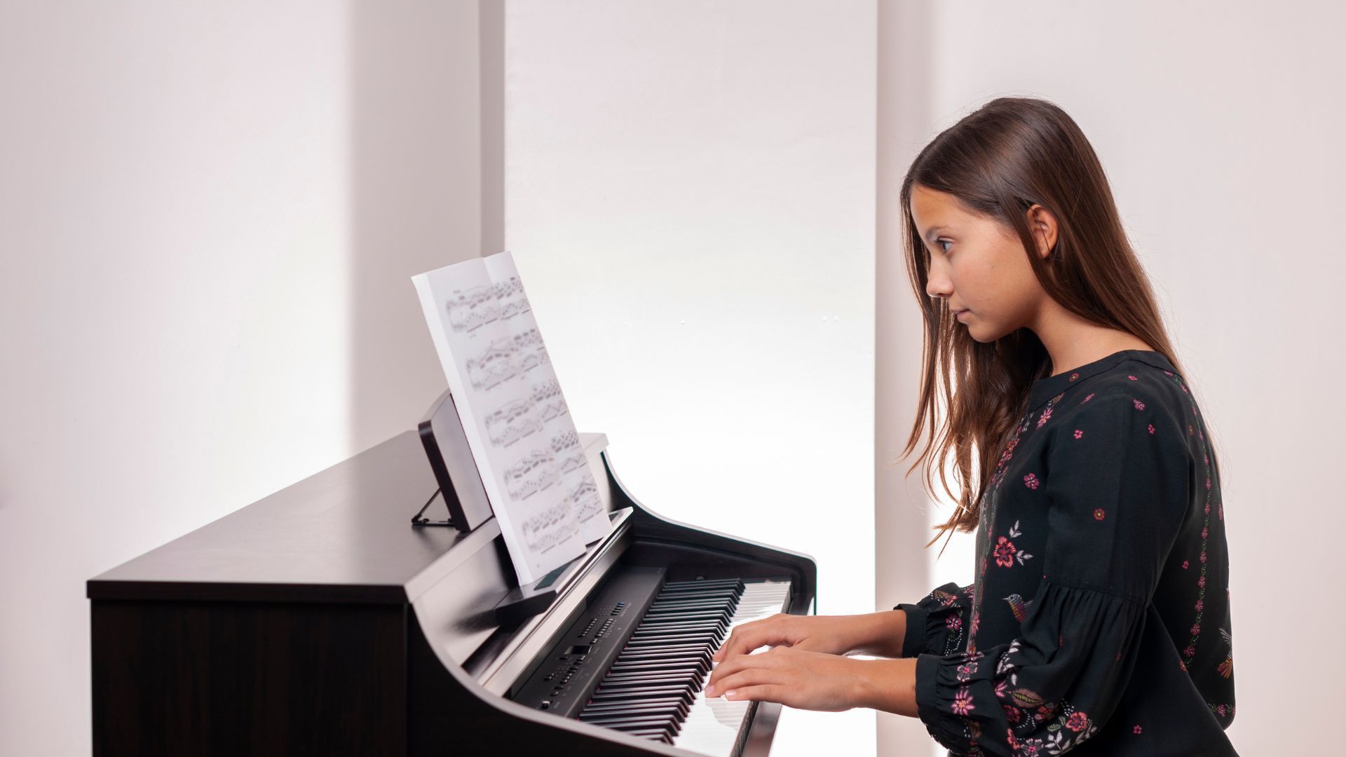 Girl playing piano, reading sheet music in a white room.
