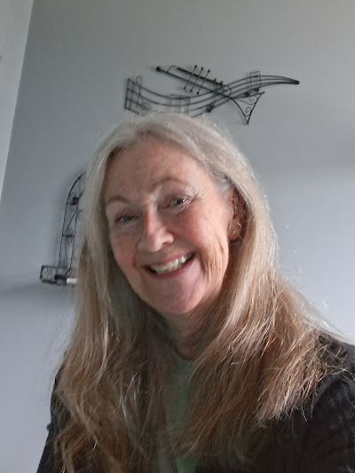 Woman with long, light hair smiles at the camera. A musical note wall art is visible in the background.