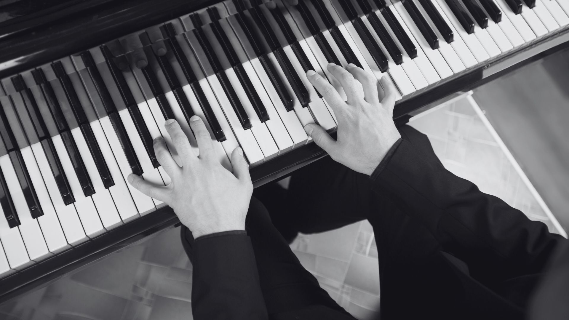 Hands playing a piano; black and white.