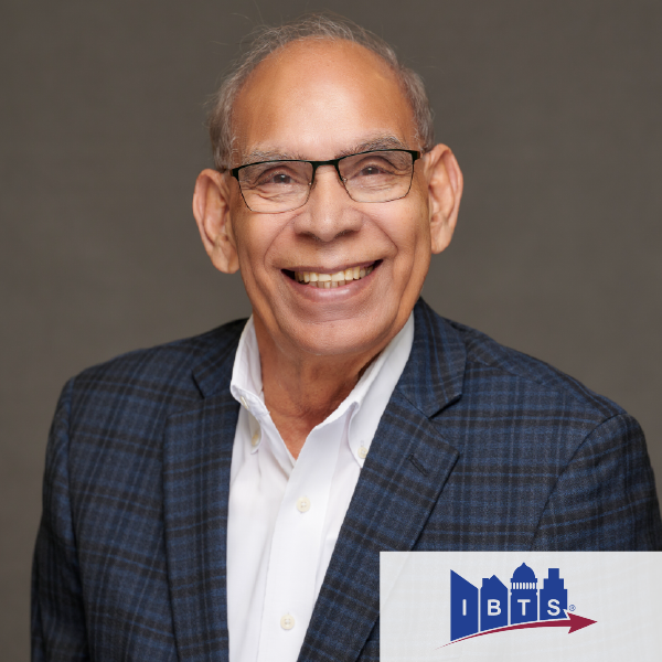 Hombre sonriente con gafas y chaqueta azul a cuadros, representando a IBTS. Fondo gris.