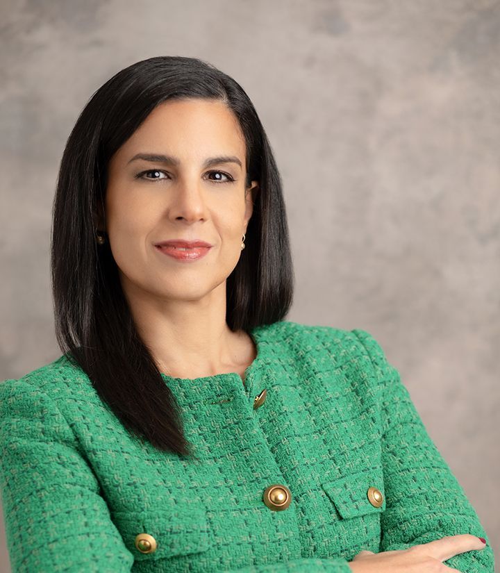 A woman in a green jacket is standing with her arms crossed.