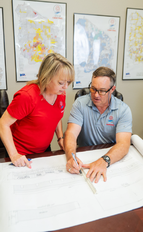 A man and a woman are sitting at a table looking at a blueprint.