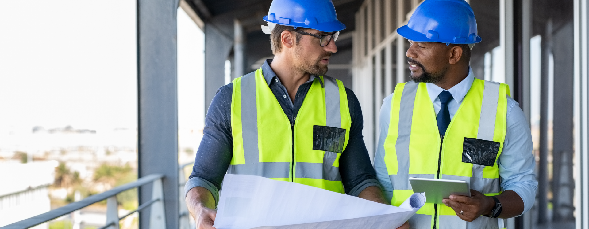Two construction workers are looking at a blueprint on a balcony.