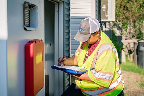 A man in a yellow vest is writing on a clipboard in front of a building.