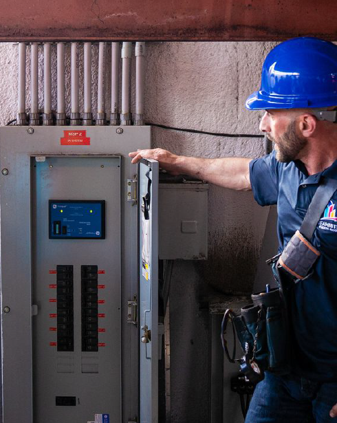 A man wearing a blue hard hat is standing in front of an electrical box.