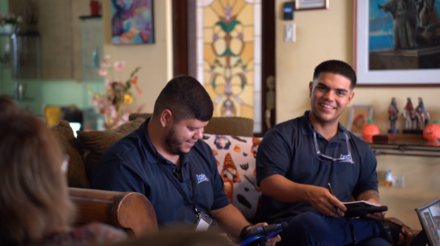 Two men are sitting on a couch in a living room looking at a tablet.
