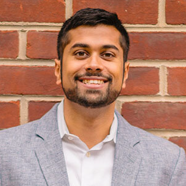 A man with a beard is smiling in front of a brick wall.